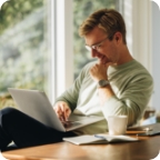 Man sits and smiles while holding laptop.